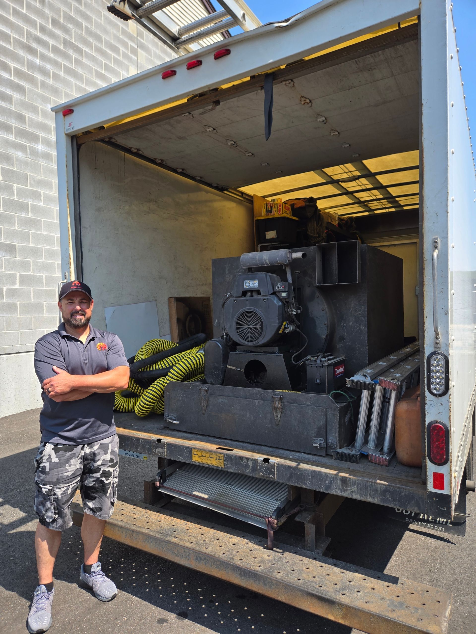 A man stands with arms crossed in front of a truck with a large machine inside.