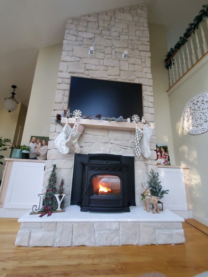 Fireplace with lit fire, mounted TV, stone surround, decorated for Christmas.