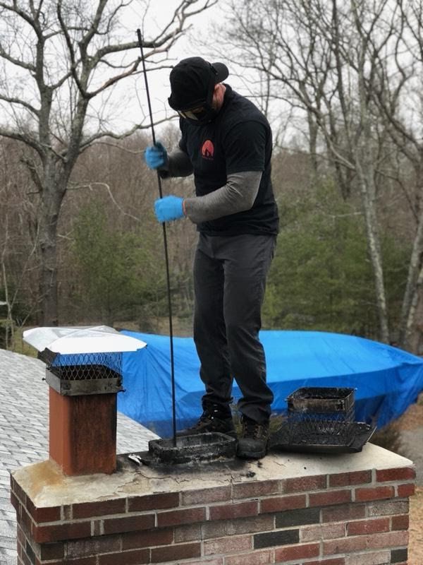 Man in safety gear cleaning a chimney. Outdoors, overcast day.