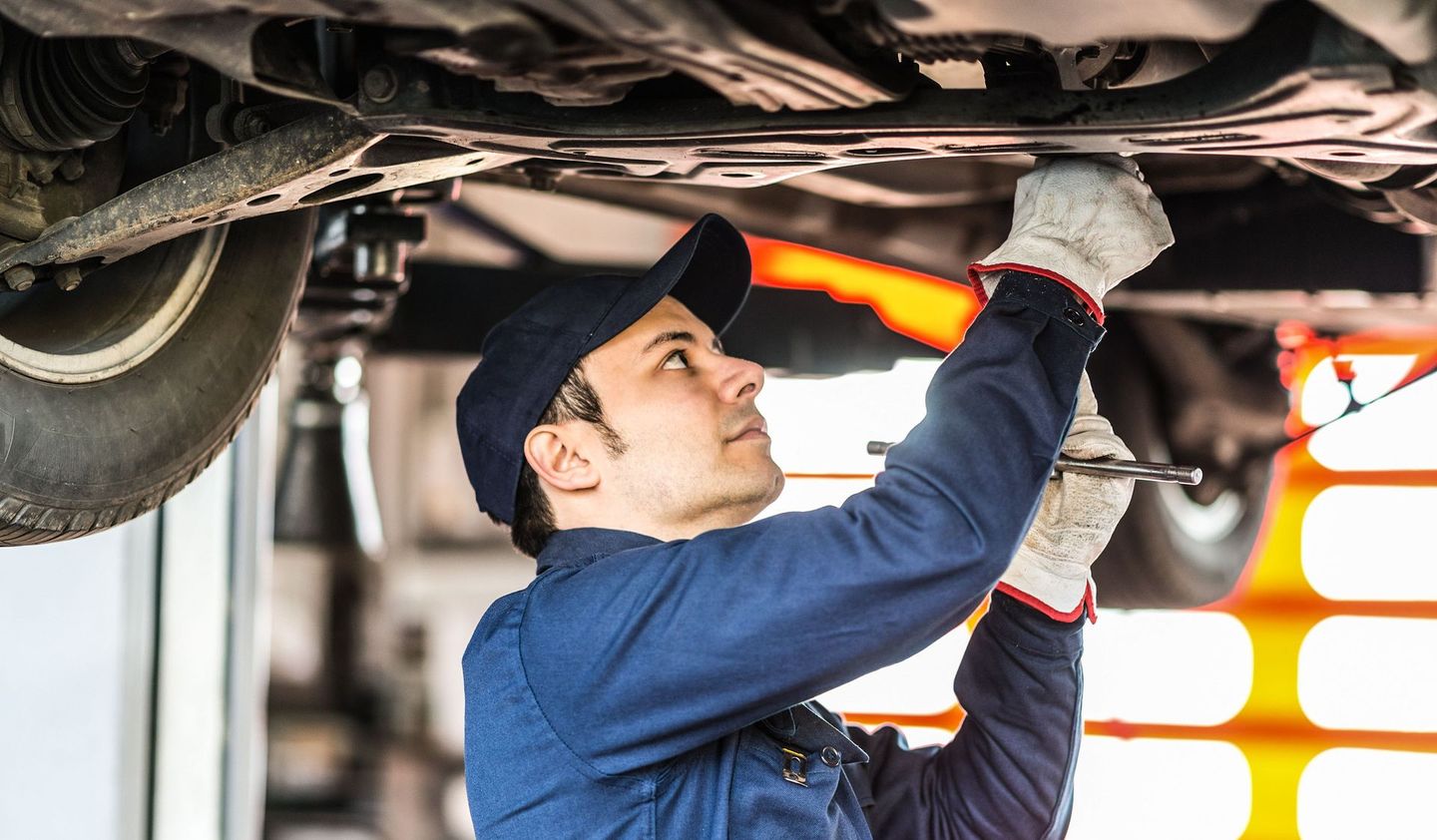 Auto mechanic working underneath a lifted vehicle, using a wrench to perform maintenance.