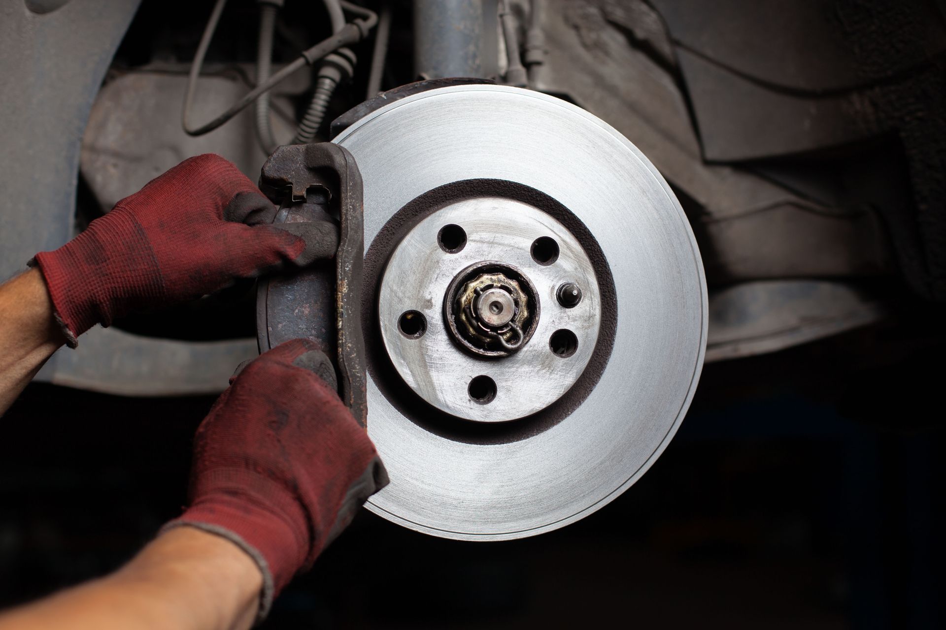 Mechanic wearing red gloves installing or inspecting a car brake disc and caliper.