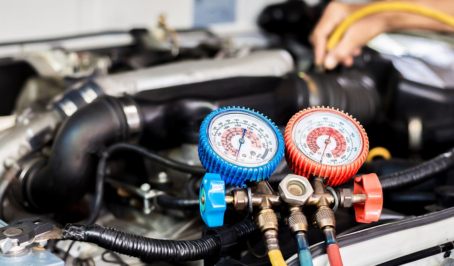 Close-up of automotive air conditioning manifold gauges with red and blue dials connected to a car engine during an AC system check.