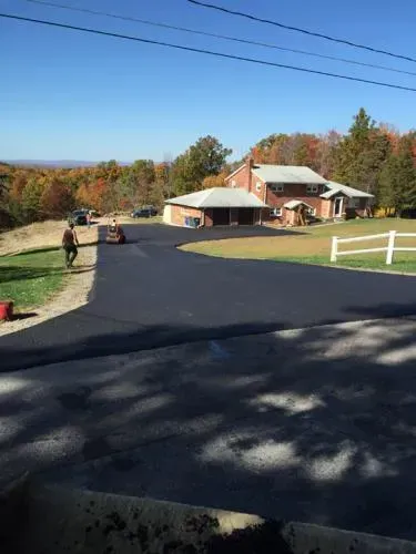 Asphalt driveway leading to a brick house with detached garage; person walking nearby. Autumn landscape.