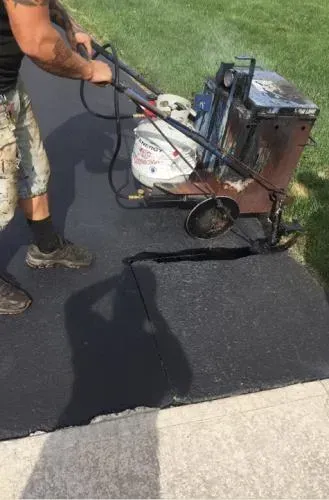 Man using a propane-powered asphalt repair machine on a black surface.