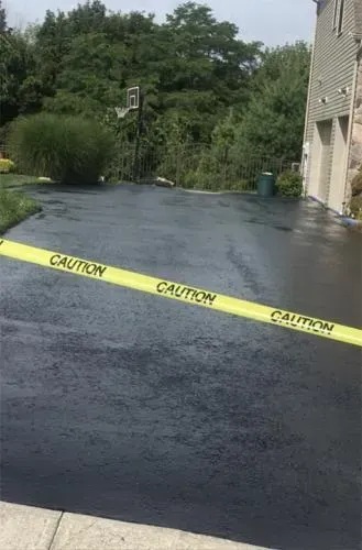 Freshly sealed black asphalt driveway with caution tape.