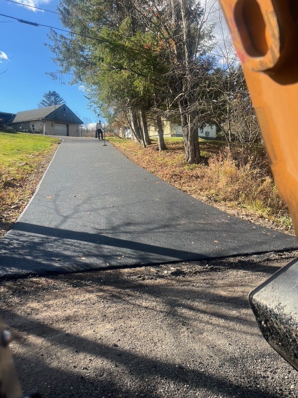 A newly paved asphalt driveway leading uphill towards a building on a sunny day.