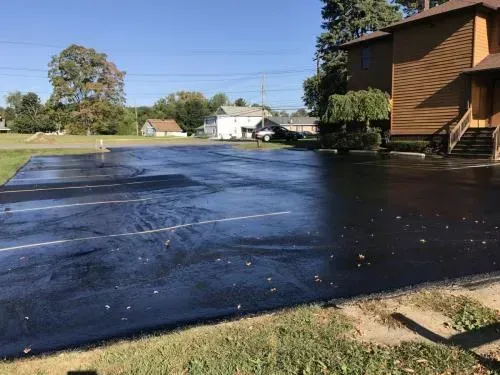 Newly paved asphalt parking lot next to a two-story wooden building on a sunny day.