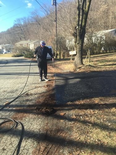 Person spraying water on asphalt road and adjacent dirt area.