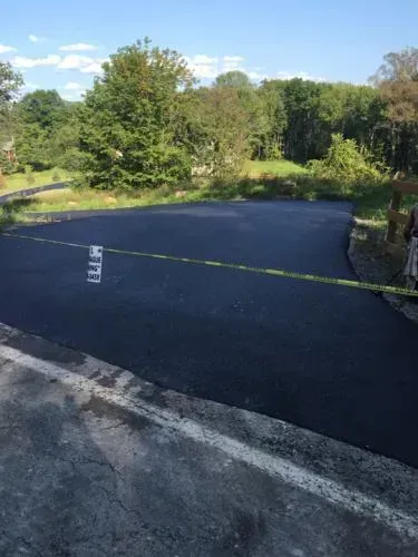 Freshly paved black asphalt driveway, with trees in the background, blocked by yellow caution tape.
