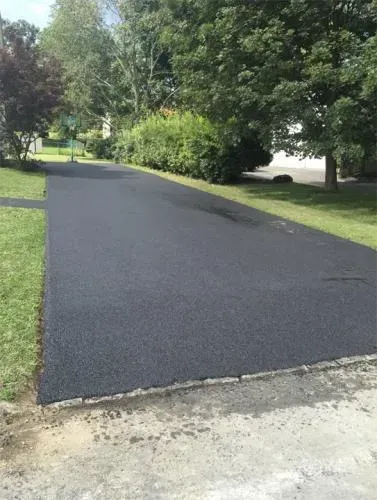 Newly paved asphalt driveway with green grass and trees in the background.