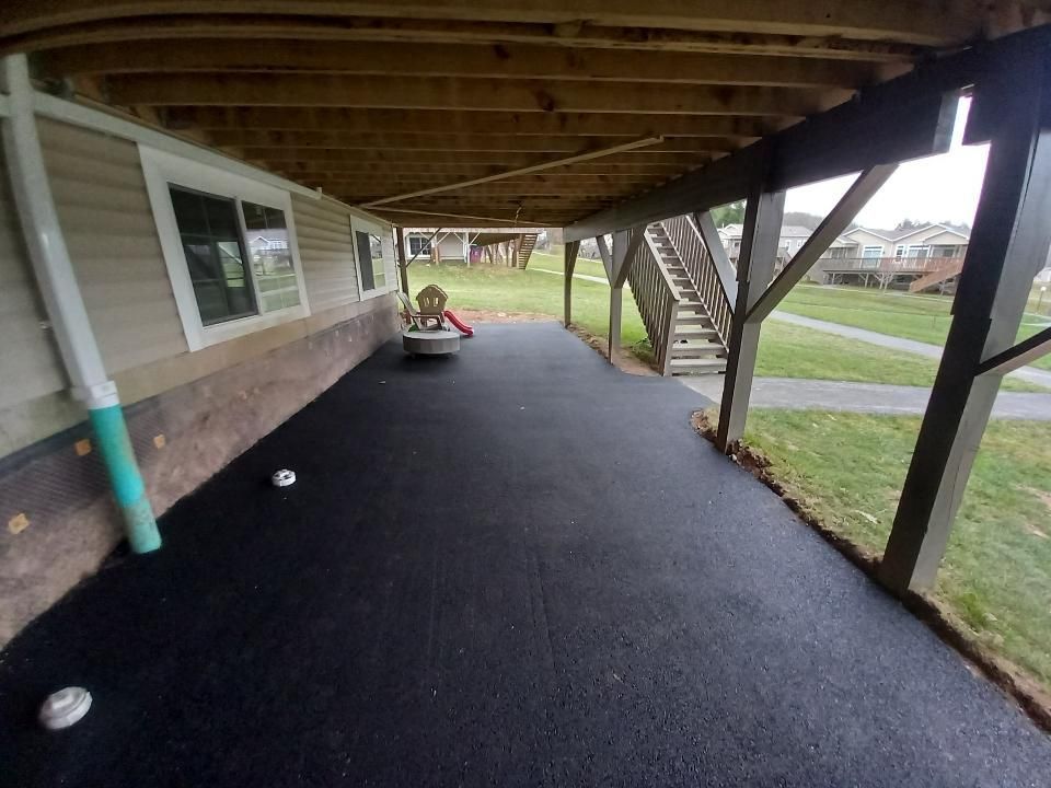 Covered outdoor patio with black surface, wooden supports, and stairs leading up.