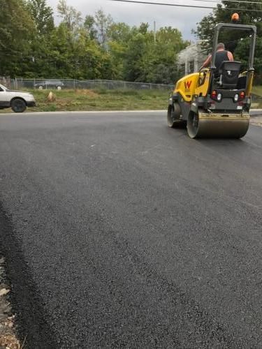 Asphalt roller compacting freshly paved road; operator in seat.