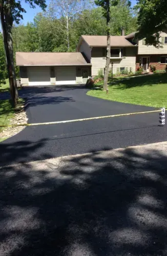 Newly paved black asphalt driveway leading to a two-story house with a garage.