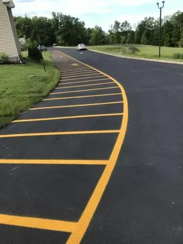 Asphalt road with yellow crosshatched markings curving to the right. Green grass and trees border the road.