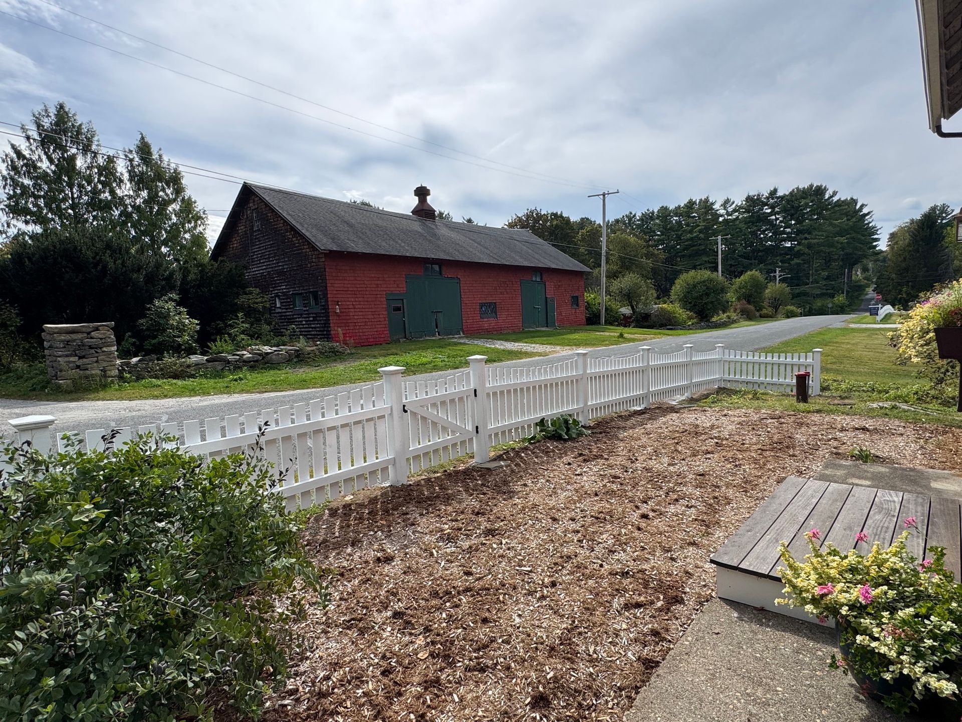 Red barn with green doors behind a white picket fence on a roadside.