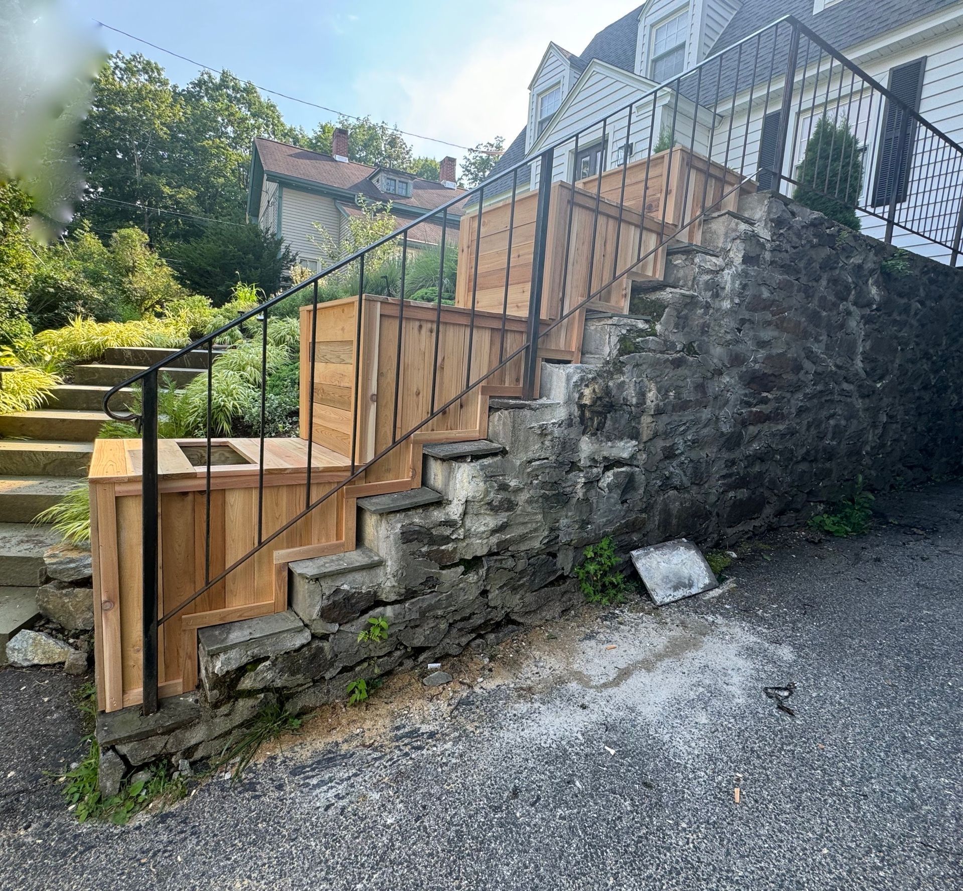 Staircase with wooden planters and a black metal railing against a stone wall.