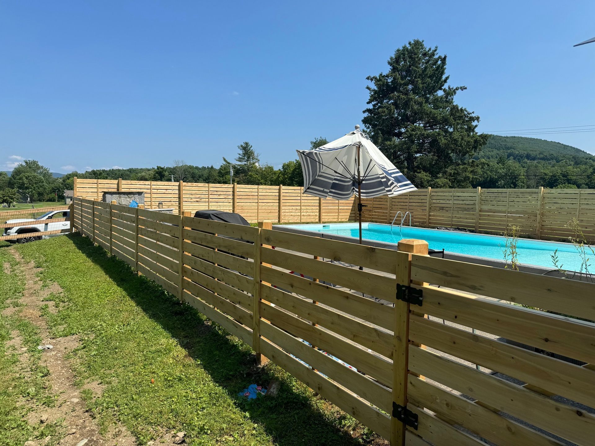 Wooden fence surrounds a pool on a sunny day.