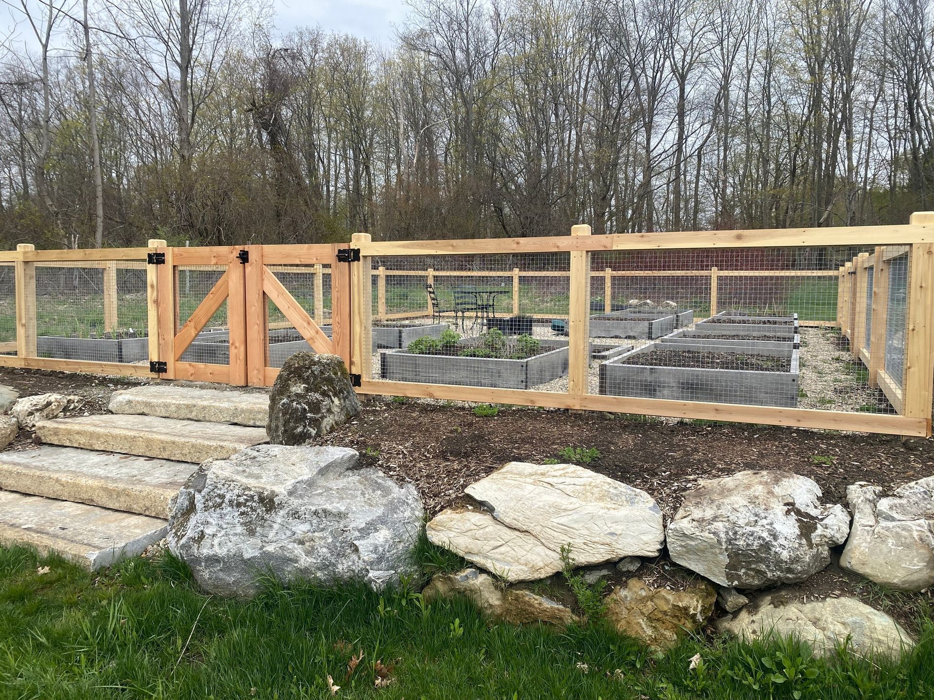 Garden with raised beds, fenced in with a wooden gate and stone steps leading to the garden.