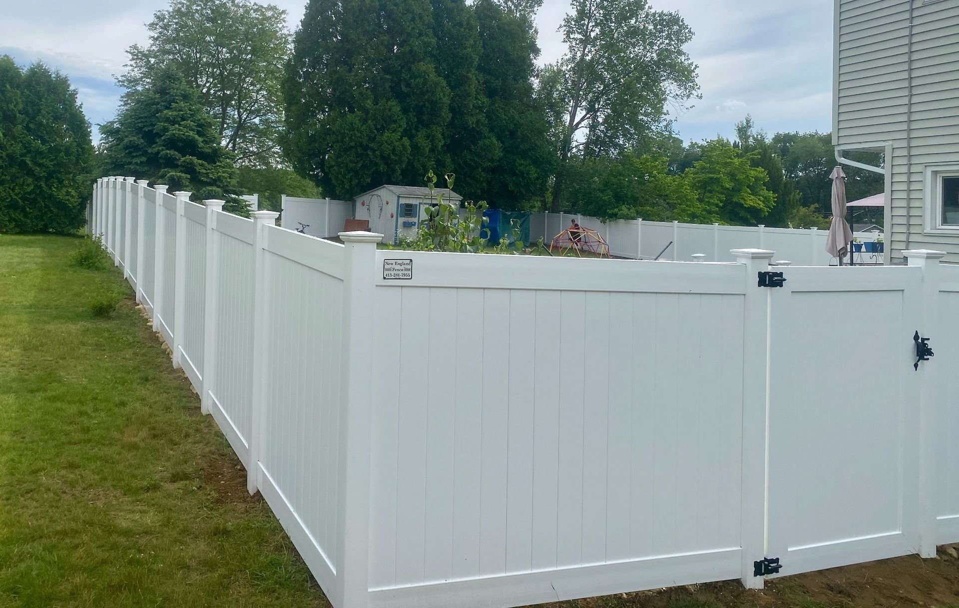 White vinyl fence encloses a backyard with grass, trees, and a shed. Gate visible.
