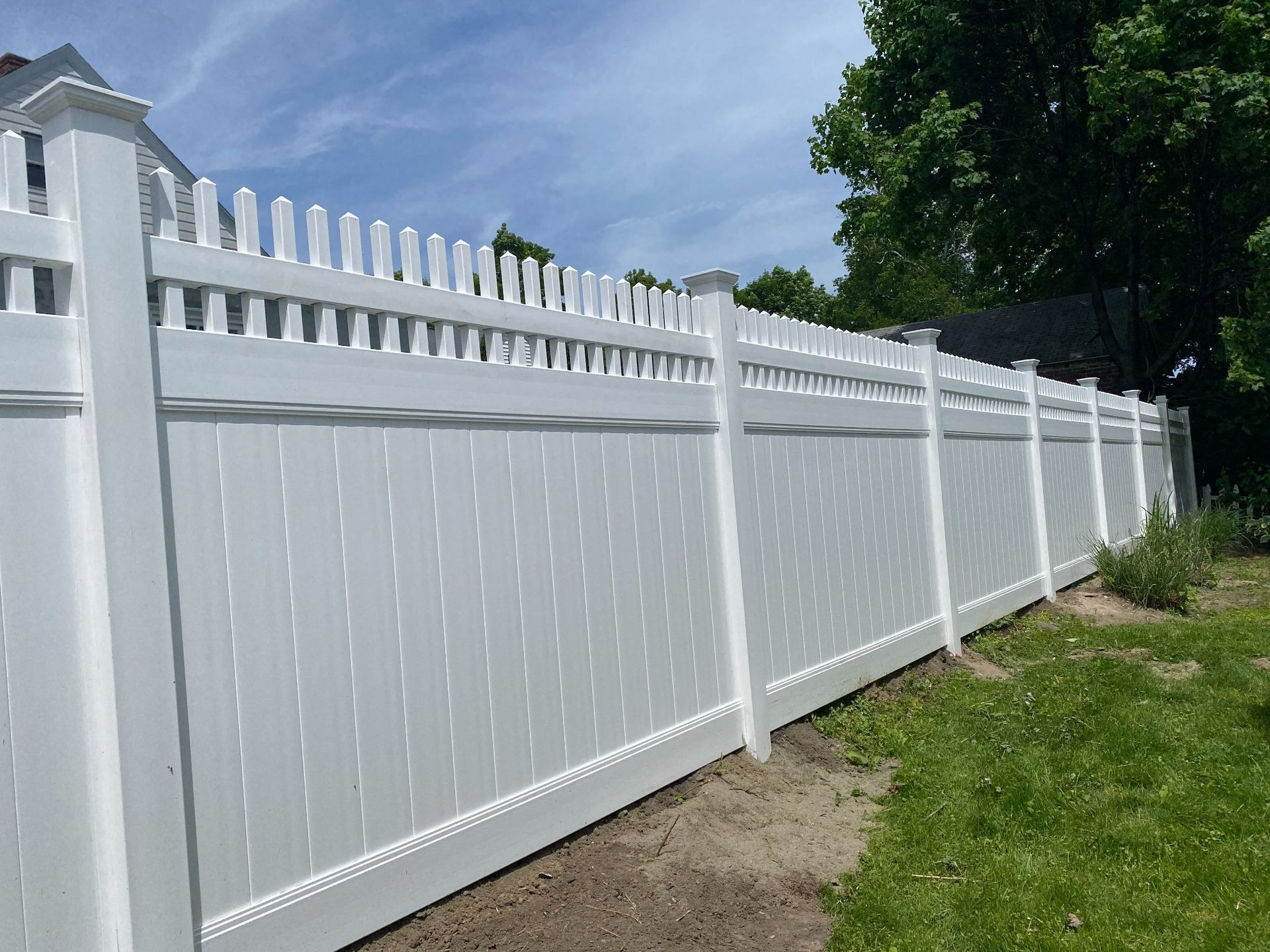 White vinyl fence with picket top in a yard on a sunny day.