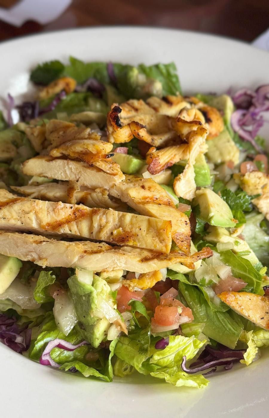 A salad with chicken, lettuce, tomatoes, and avocado on a plate