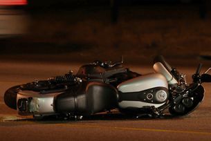 A motorcycle is laying on its side on the side of the road.