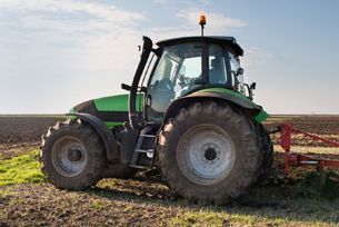 A green tractor is plowing a field with a plow.