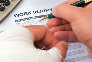A person with a bandaged hand is filling out a work injury form.