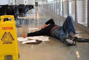 A man is laying on the floor next to a caution sign.