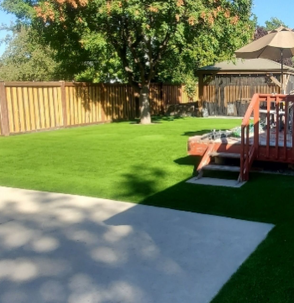Backyard with green lawn, wooden fence, and a deck with steps and patio umbrella