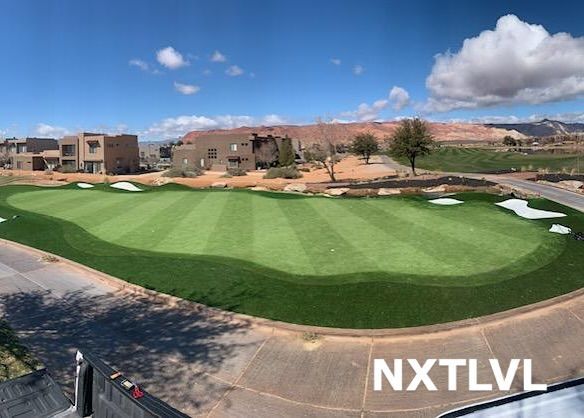 Golf course green with sand bunkers, desert buildings, and blue sky with clouds