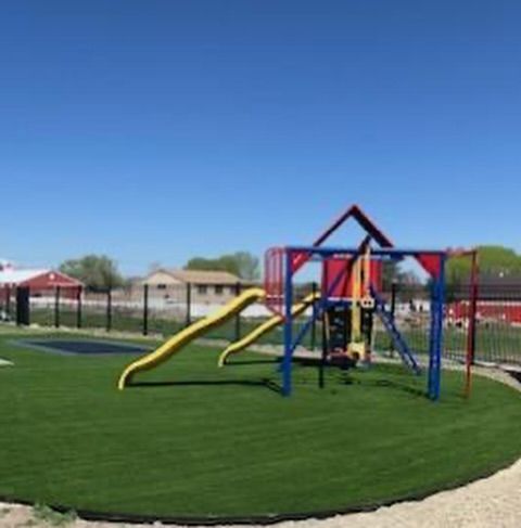 Playground with yellow slides and blue climbing frame on green turf under a clear sky