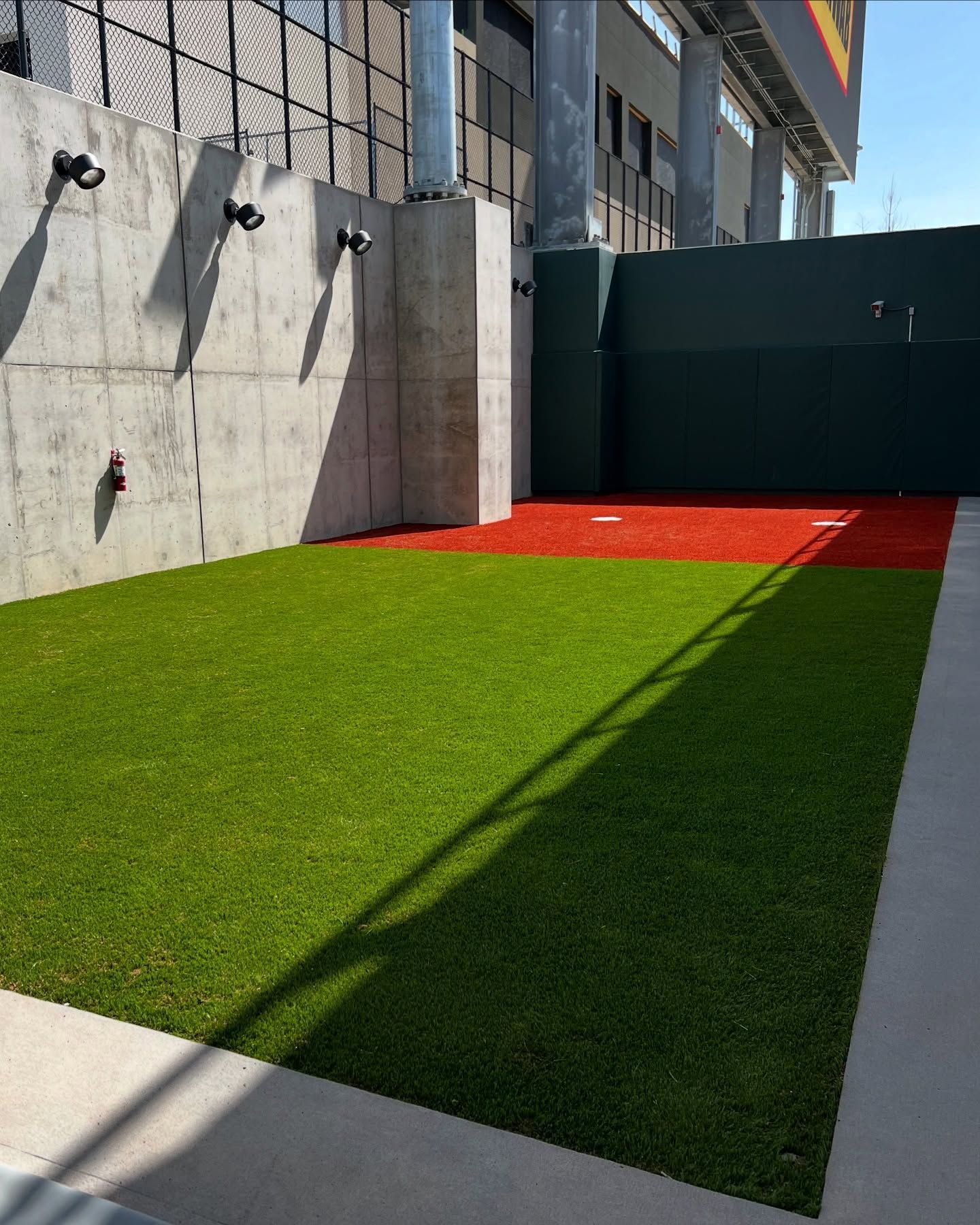 Small outdoor courtyard with green turf, red corner, and concrete walls beside a building.