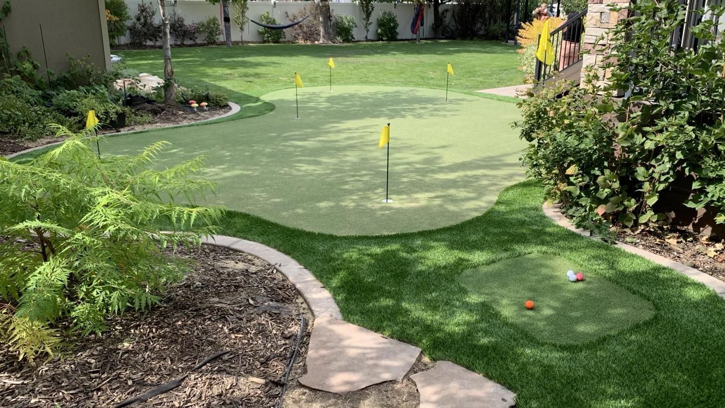 Backyard putting green with hole markers, bordered by plants and a stone path