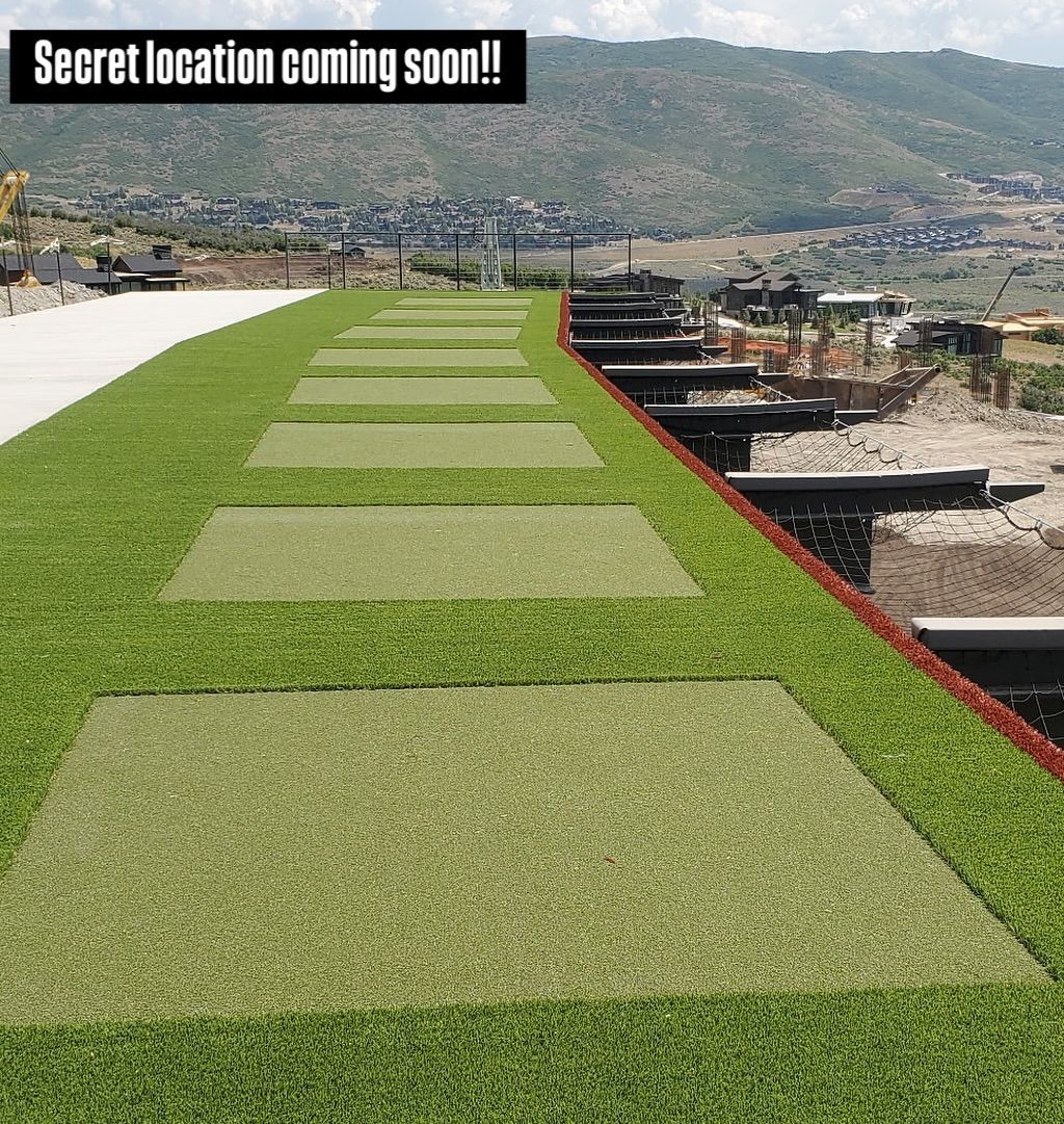 Rooftop grass walkway with rectangular patches and a “Secret location coming soon!” banner overlooking hills.