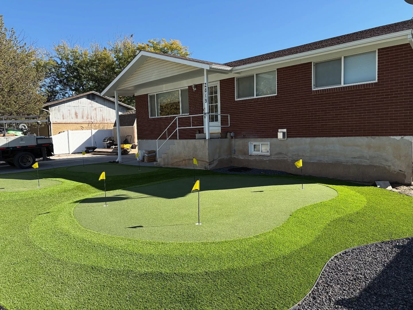 Front yard with a circular artificial putting green and small flags beside a red house