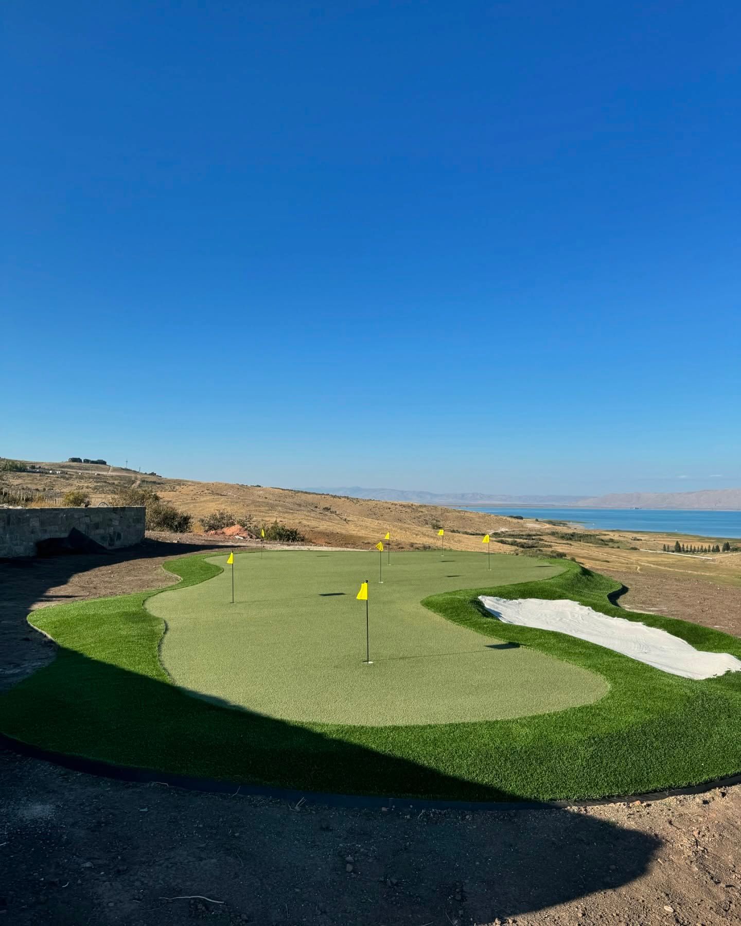 Golf putting green by the sea under a clear blue sky.