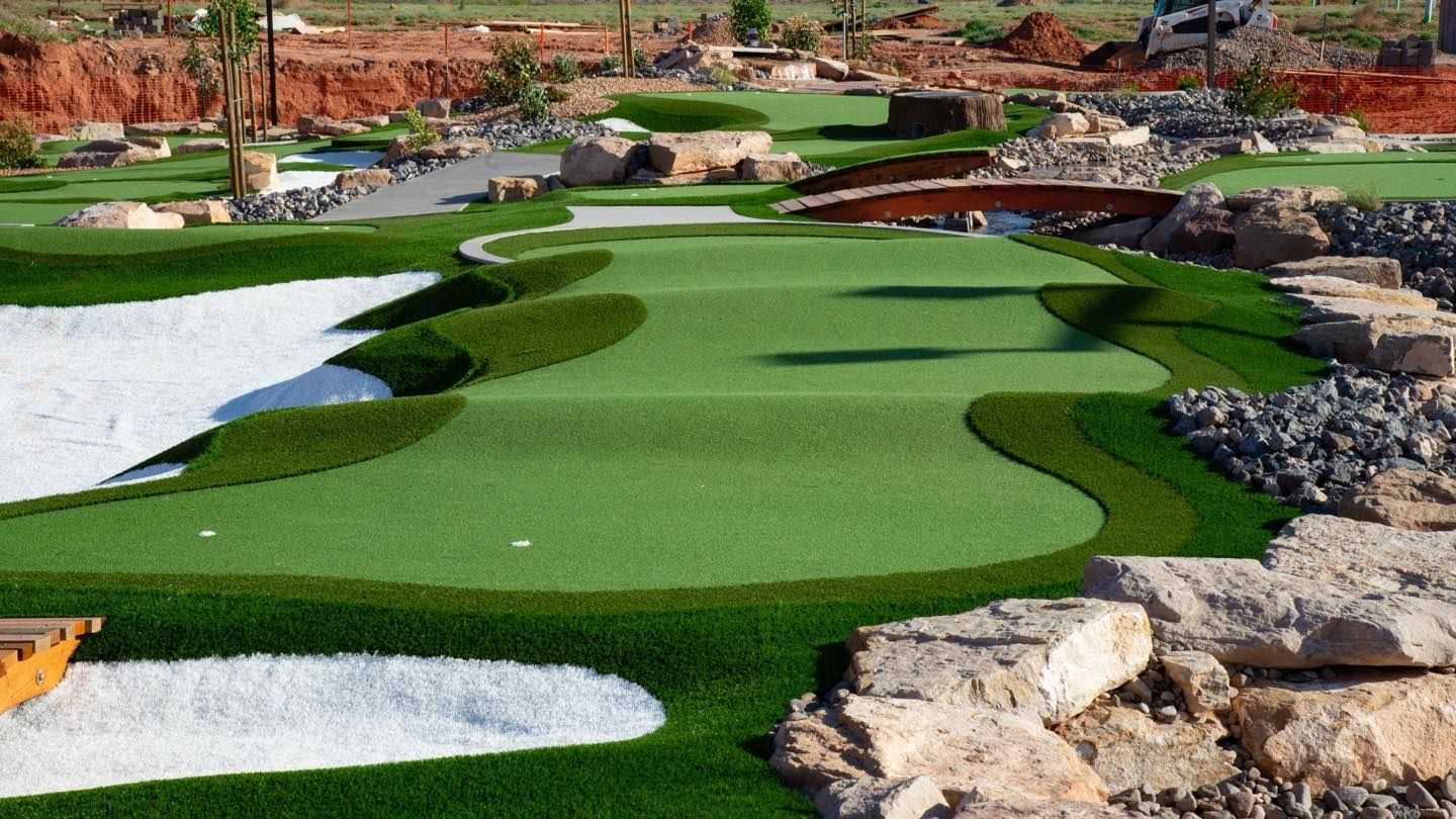 Mini golf course with bright green turf, white sand bunkers, and rocky desert landscaping