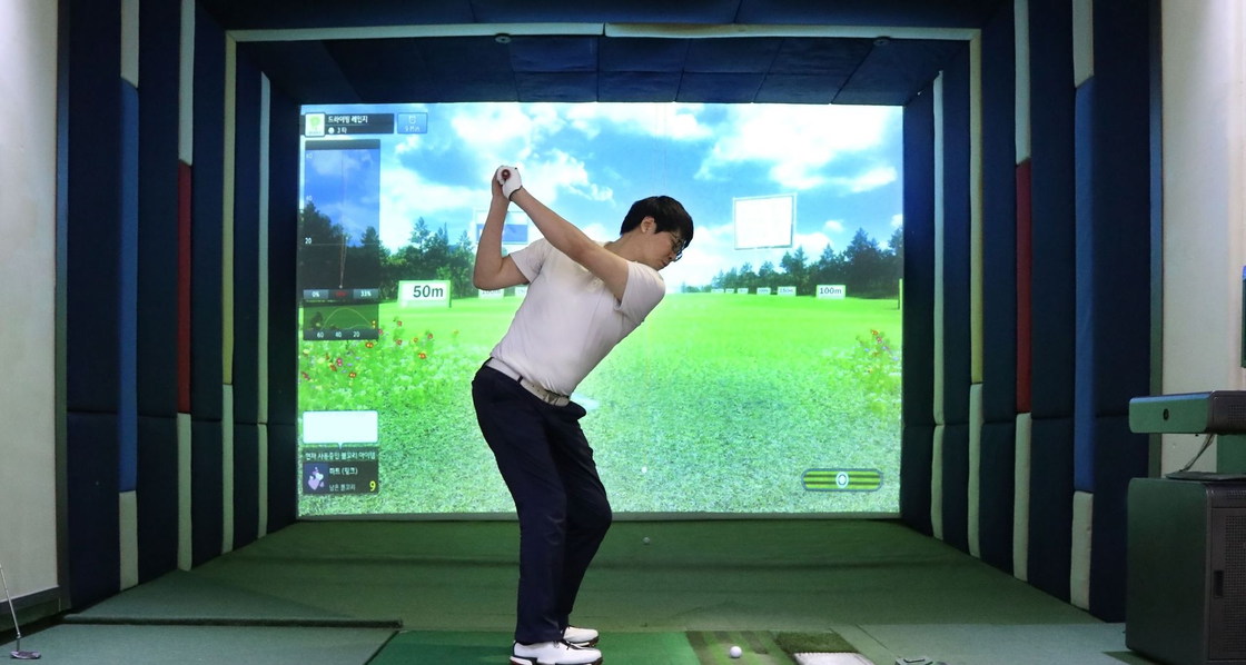 Man swinging a golf club indoors in a simulator with a bright virtual fairway screen