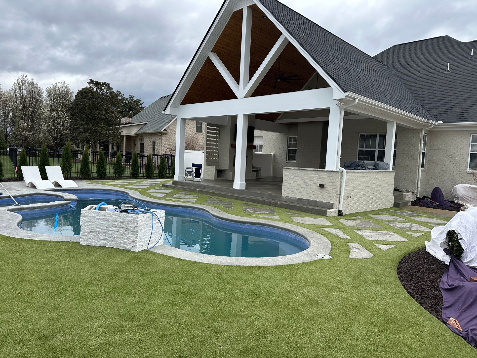 A backyard featuring a pool, stone patio, and a covered outdoor living area with a fireplace under a vaulted ceiling.