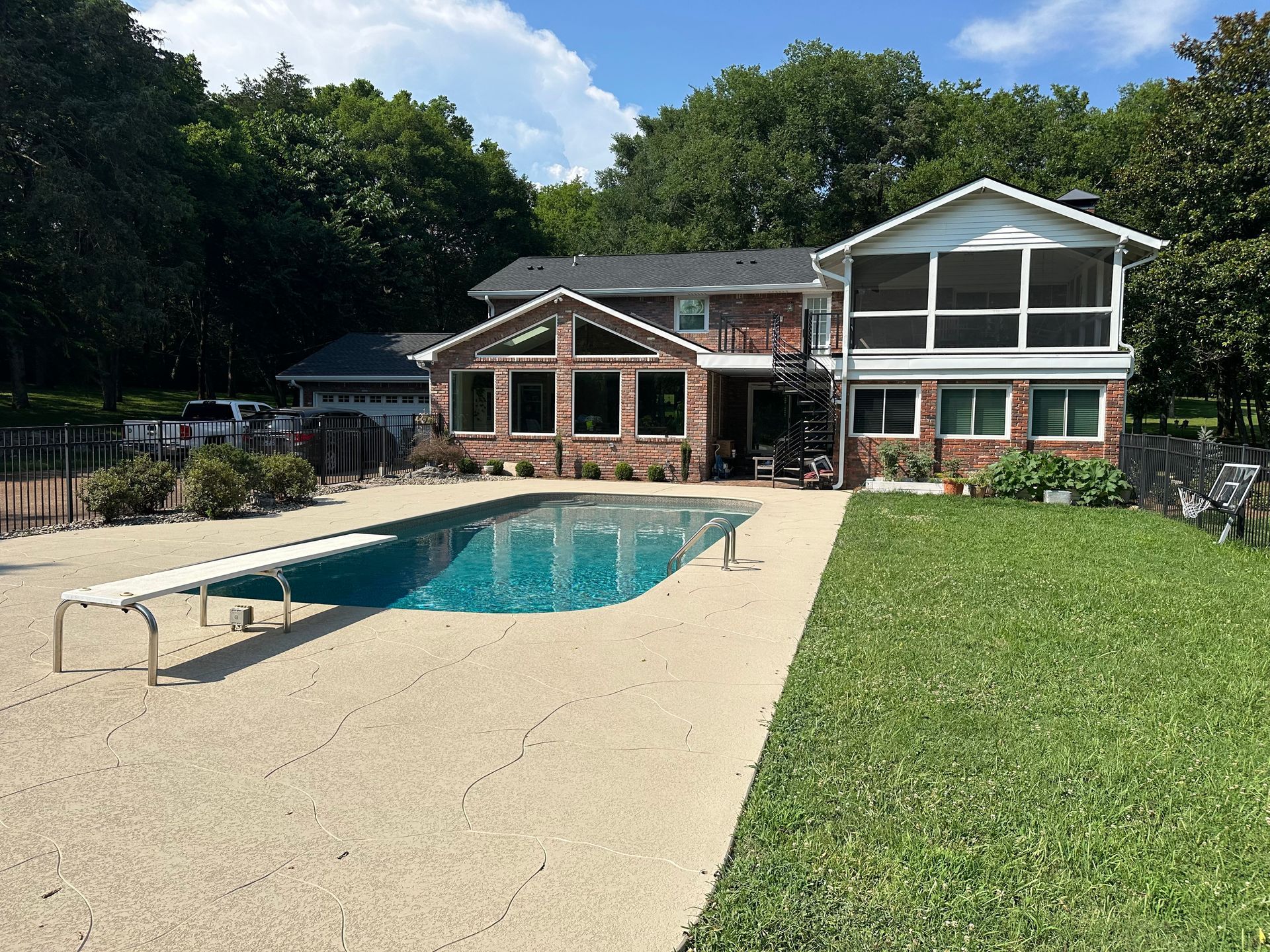 A brick house with a screened porch and a swimming pool in a grassy backyard under a blue sky.