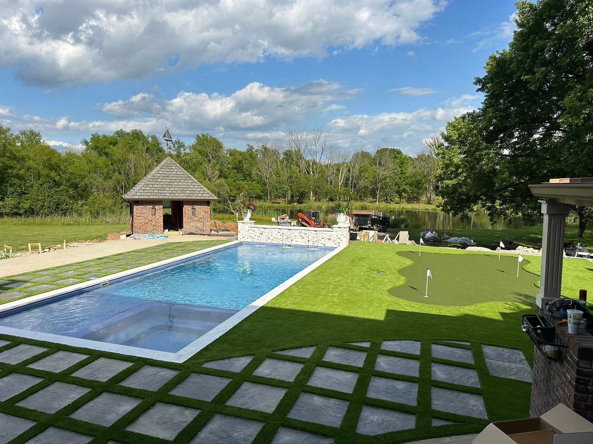 Pool and putting green in backyard with gazebo and water view on a sunny day.
