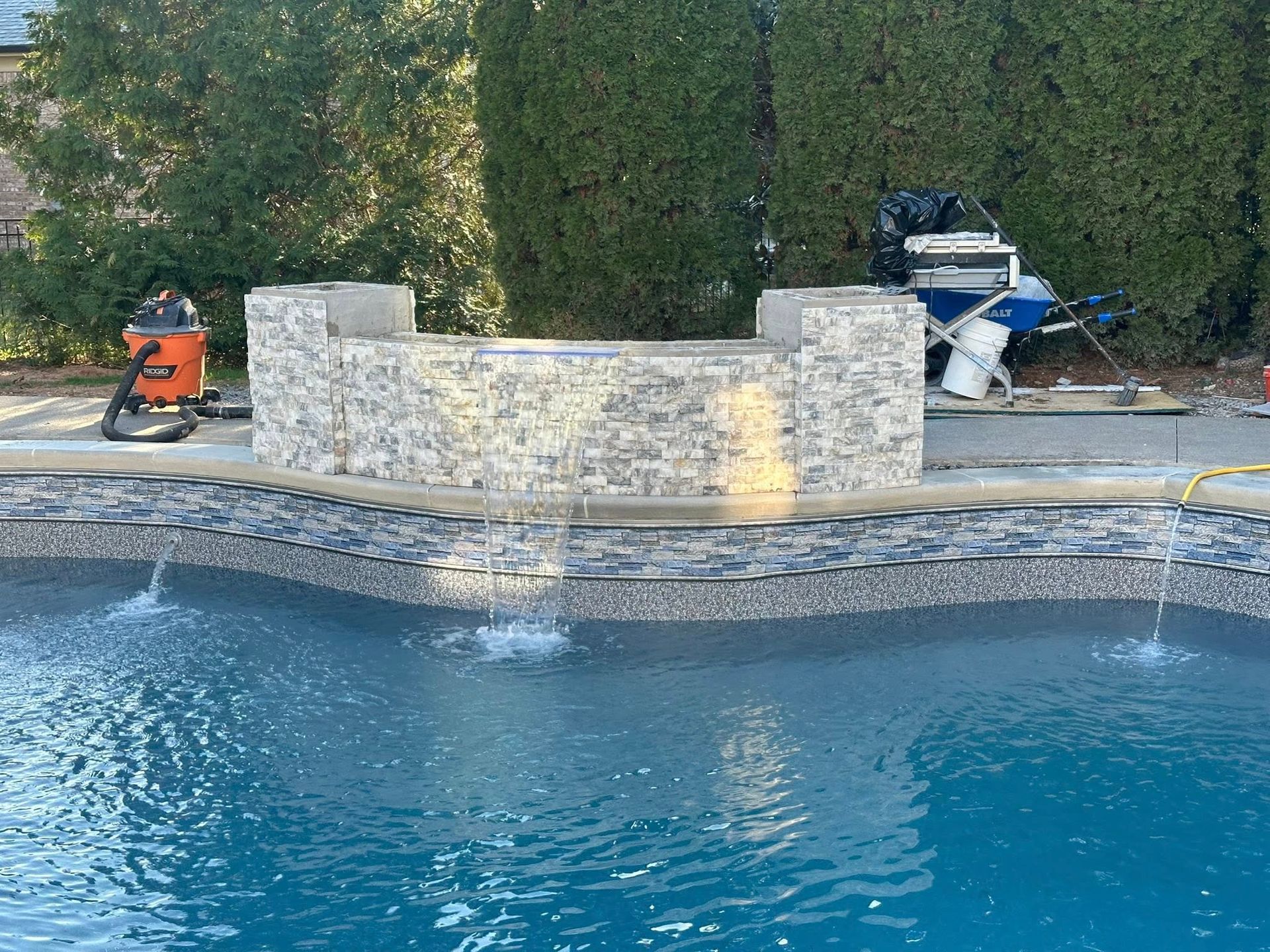 A pool with a stone fountain, water flowing. Construction equipment is nearby.