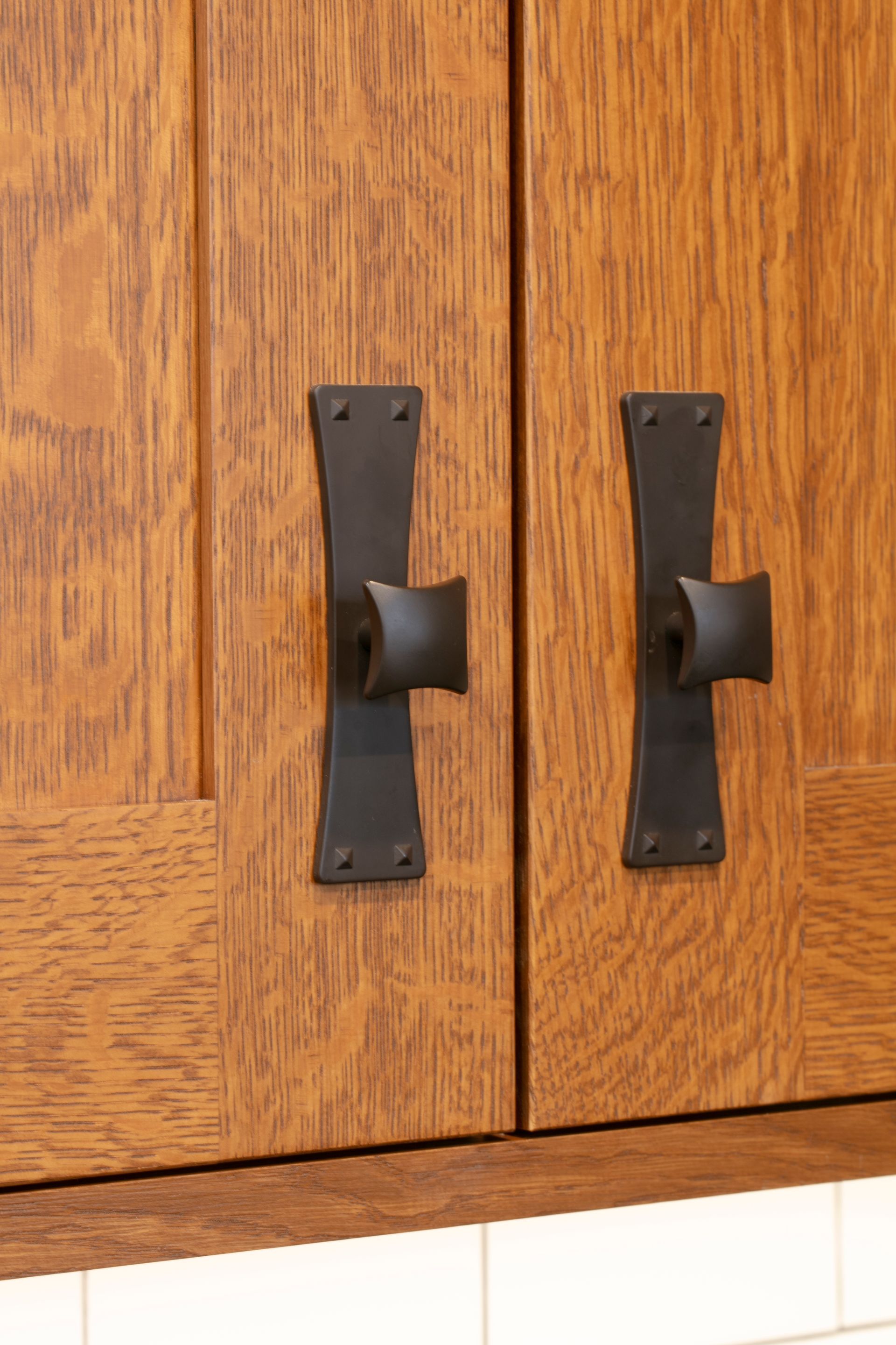 Two wooden cabinet doors with black handles and a light-colored tile backsplash.