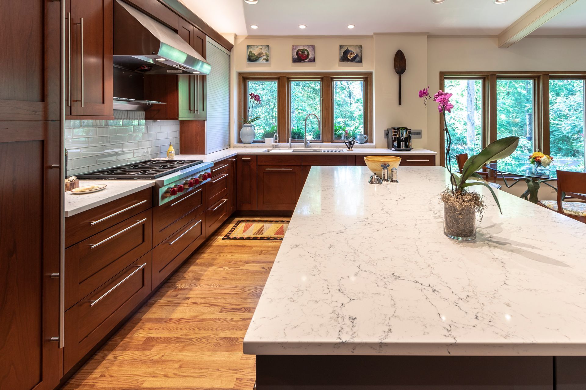 Elegant kitchen with dark wood cabinets, white countertops, and large windows overlooking trees.