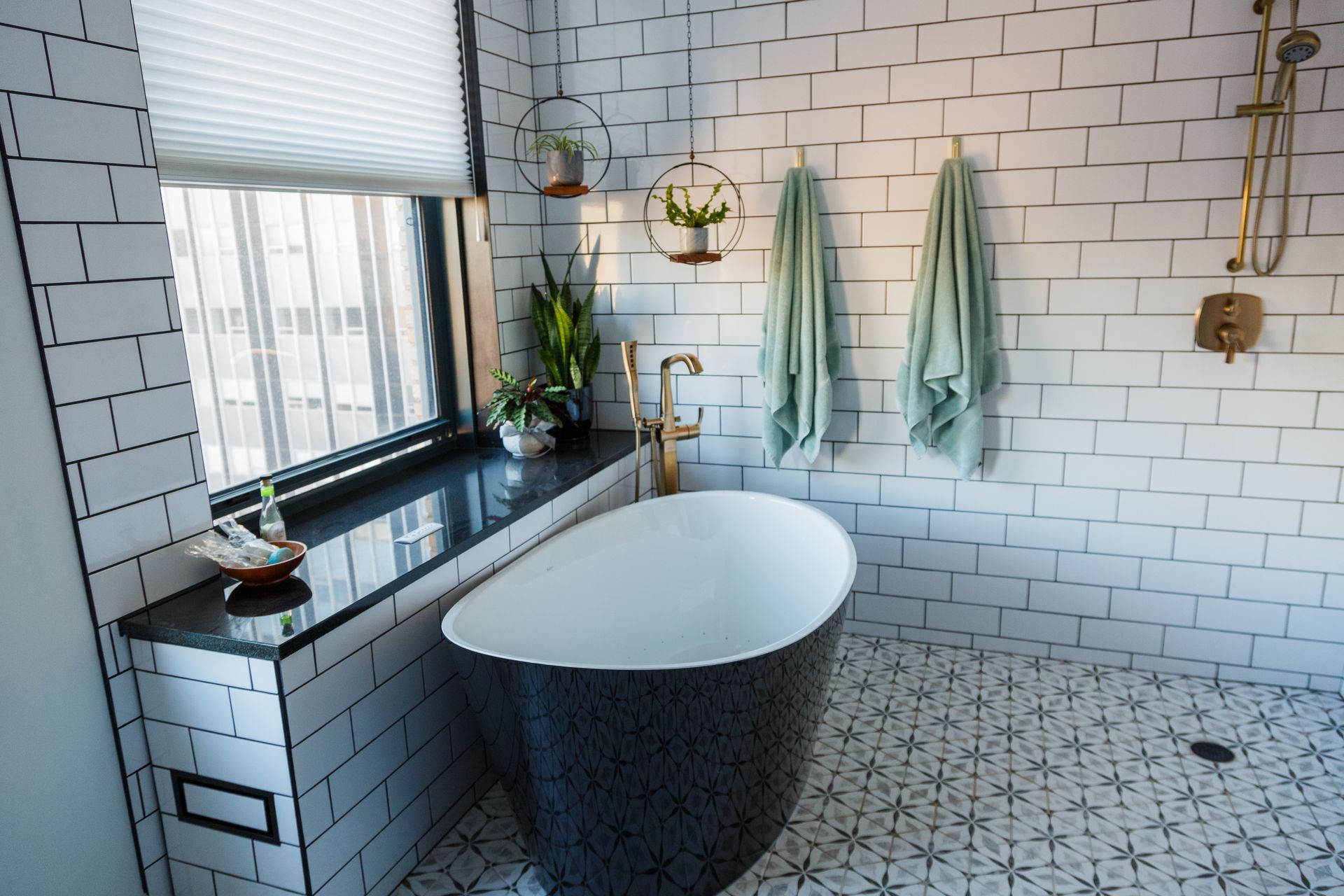 Modern bathroom with black and white tile, a freestanding tub, and gold fixtures.