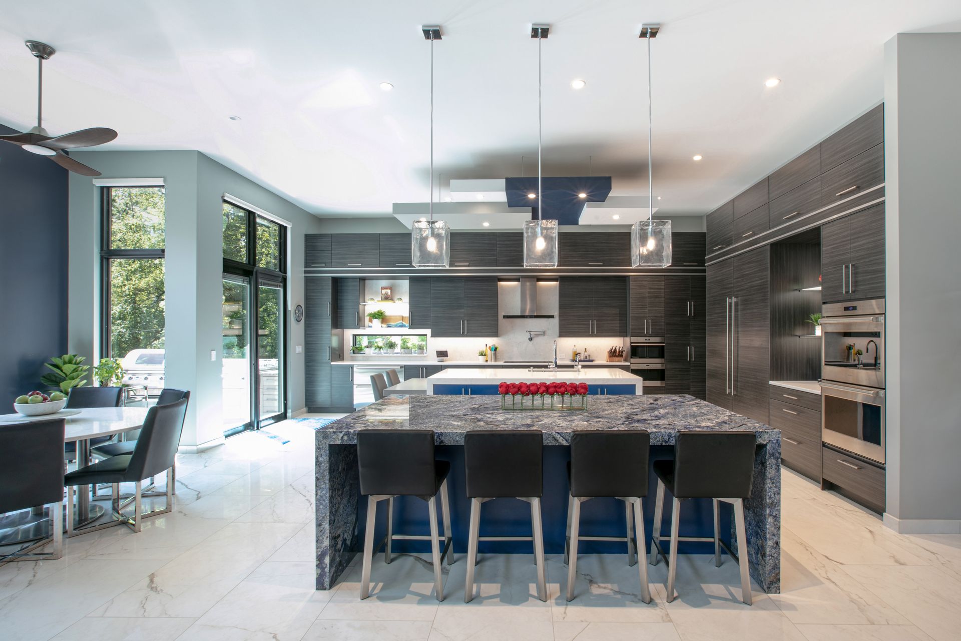 Modern kitchen with blue and gray cabinets, island with stools, and dining area.