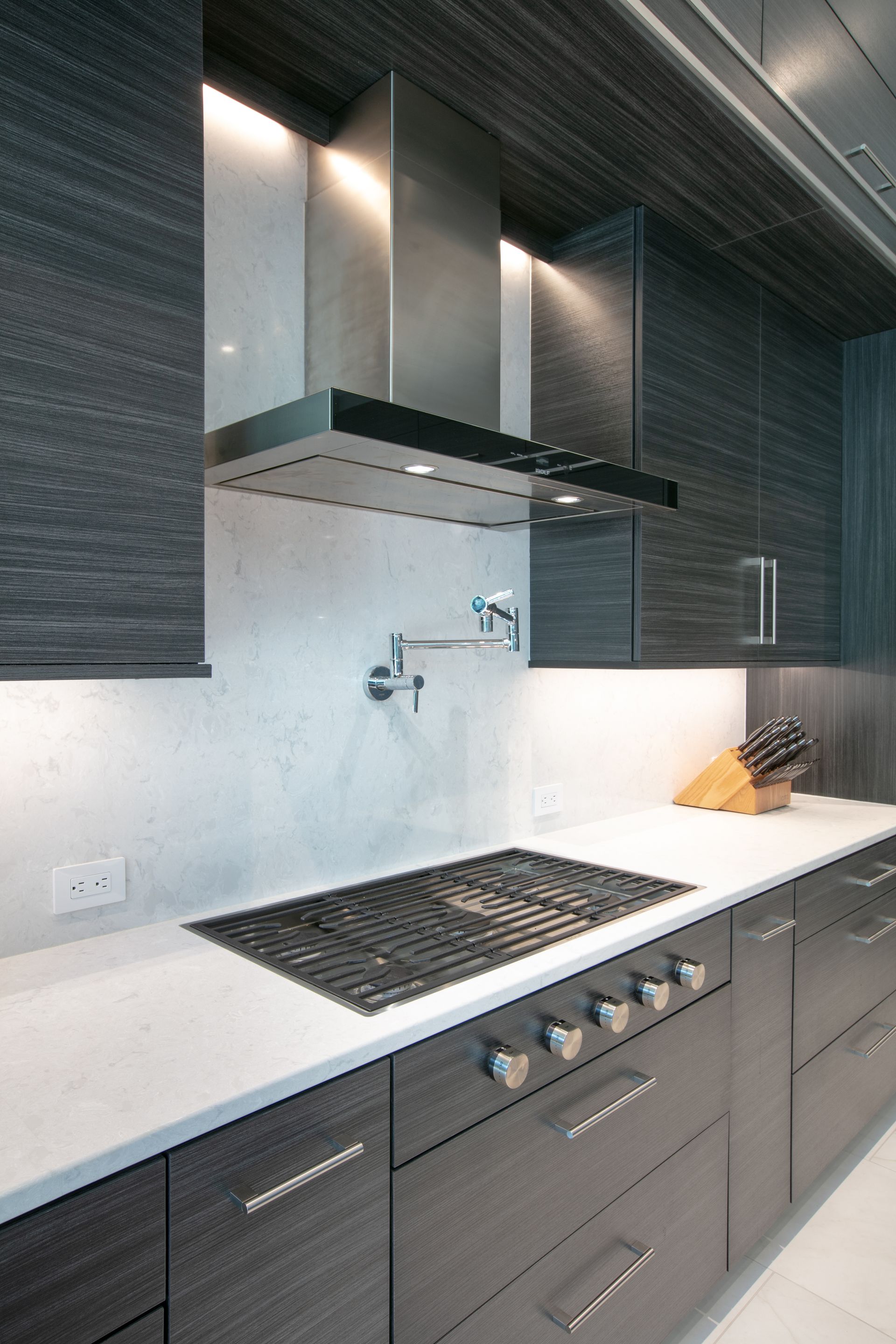 Modern kitchen with a black cooktop, stainless steel hood, and dark cabinets.
