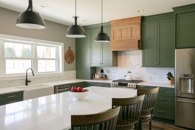 Green kitchen with island, wooden range hood, and black pendant lights.