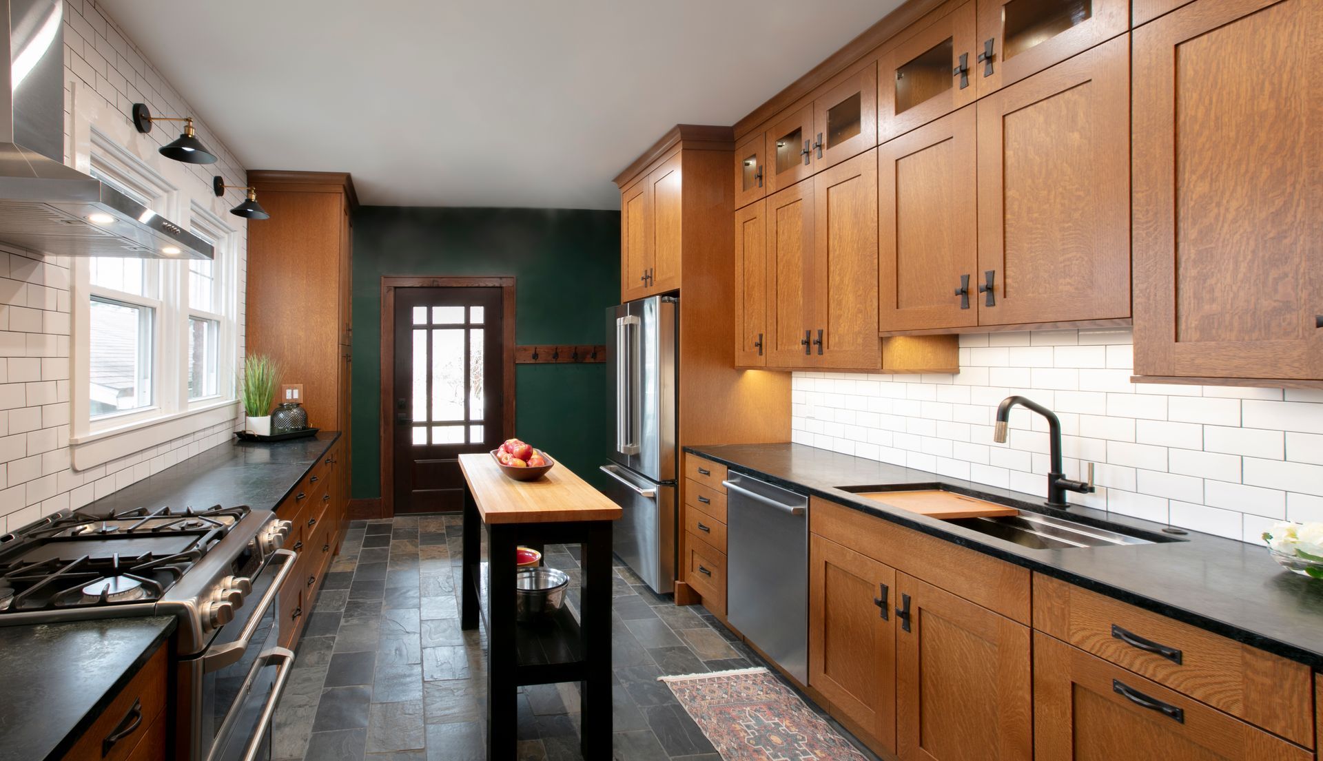 Narrow kitchen with dark countertops, wood cabinets, and a green door.